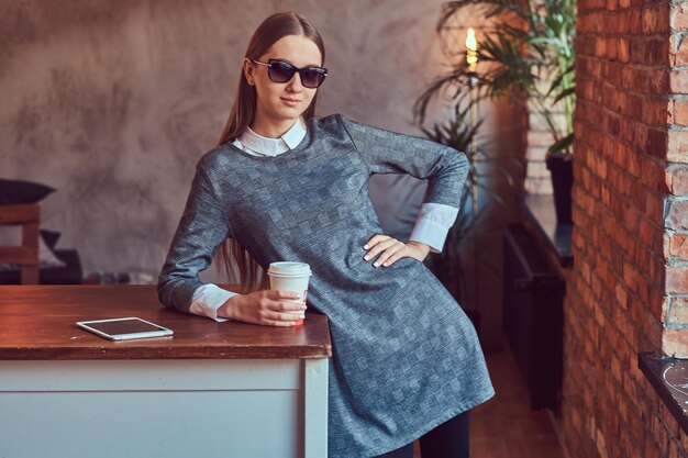 Photo gratuite une jeune fille sensuelle mince vêtue d'une robe grise et de lunettes de soleil penchées