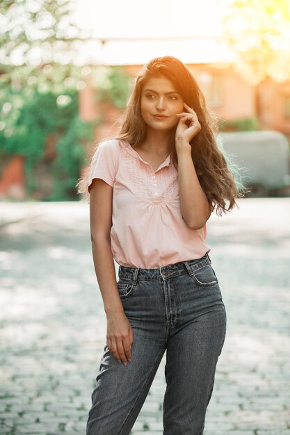 Une jeune fille sexy se tient dans la rue vêtue d'un chemisier rose pâle et d'un jean bleu