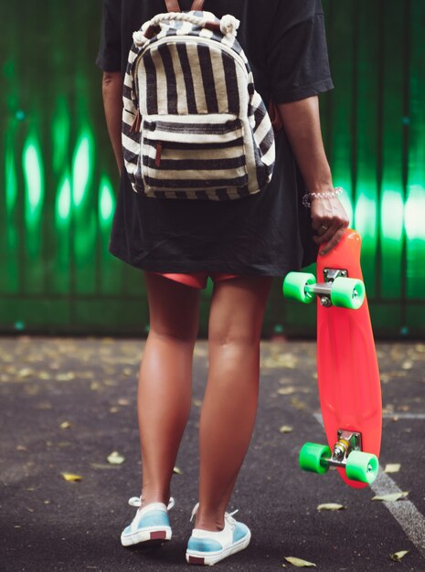 Jeune fille avec shortboard penny orange en plastique derrière le mur vert en casquette