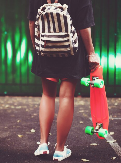 Jeune fille avec shortboard penny orange en plastique derrière le mur vert en casquette