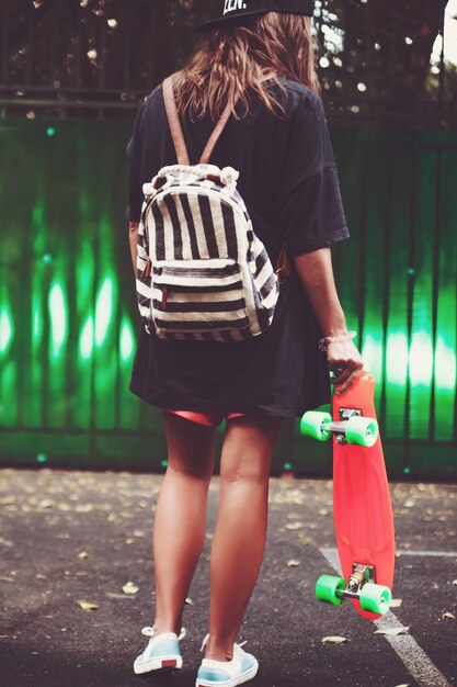 Jeune fille avec shortboard penny orange en plastique derrière le mur vert en casquette