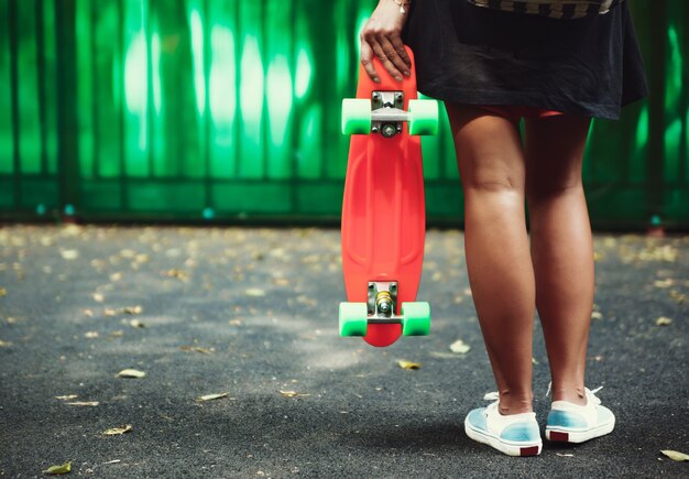 Jeune fille avec shortboard penny orange en plastique derrière le mur vert en casquette