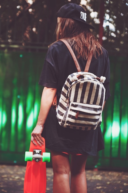 Jeune fille avec shortboard penny orange en plastique derrière le mur vert en casquette