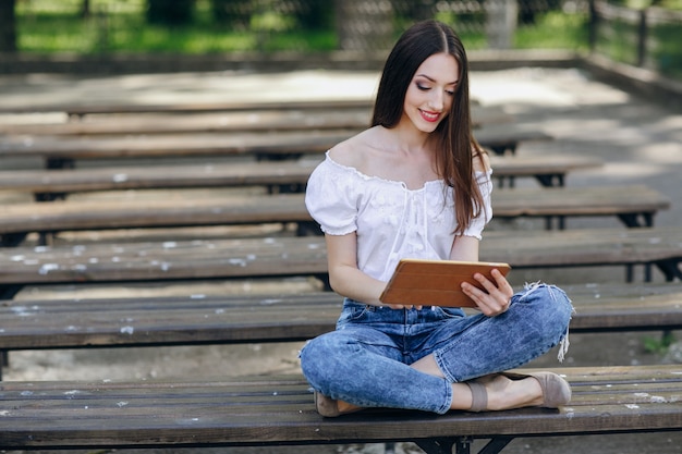 Jeune fille souriante et assis sur un banc en bois avec une tablette