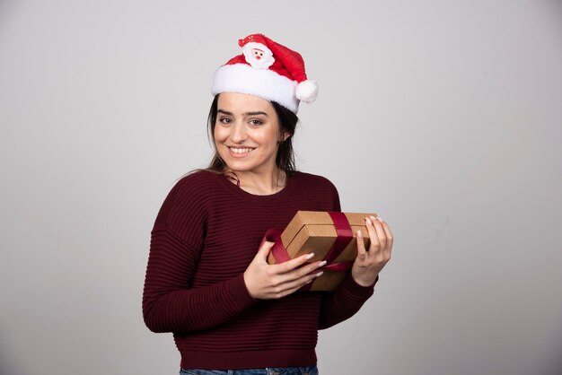 Jeune fille souriante en bonnet de Noel tenant une boîte-cadeau avec bonheur.