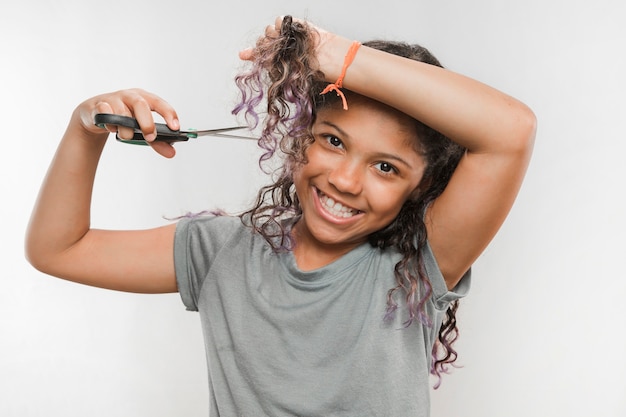 Jeune fille souriante coupe ses cheveux avec des ciseaux