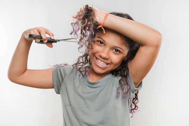 Photo gratuite jeune fille souriante coupe ses cheveux avec des ciseaux