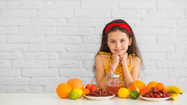Photo gratuite jeune fille souriante, debout derrière le bureau blanc avec des fruits mûrs biologiques frais et colorés