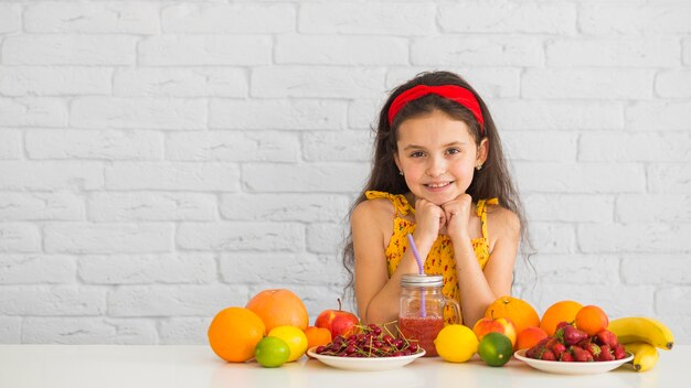 Jeune fille souriante, debout derrière le bureau blanc avec des fruits mûrs biologiques frais et colorés