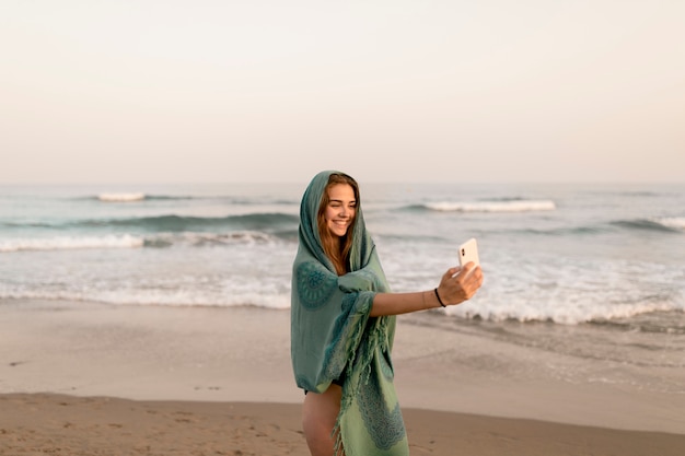 Jeune fille souriante, debout près du bord de la mer, prenant autoportrait à partir de téléphone portable