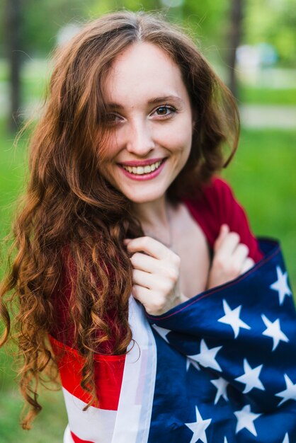 Jeune fille souriante avec un drapeau américain dans la nature