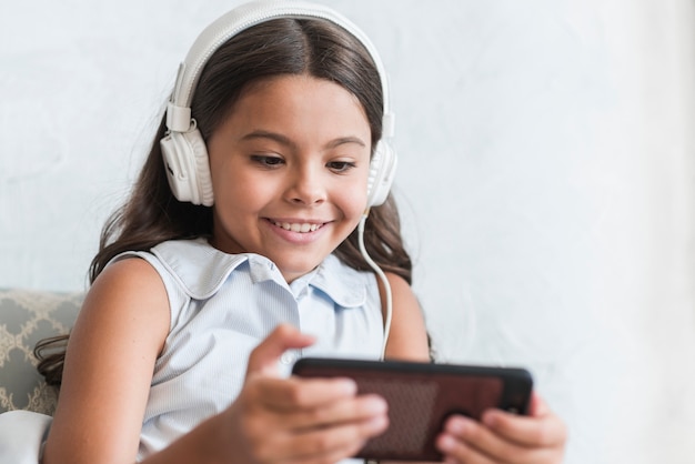 Jeune fille souriante écoute de la musique sur le casque à l&#39;aide d&#39;un téléphone intelligent