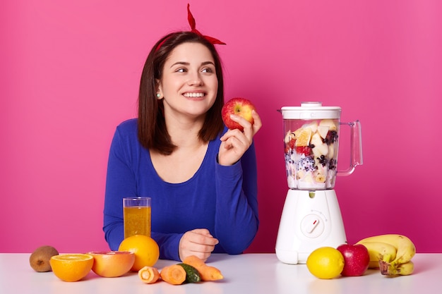 Jeune fille souriante avec des fruits frais sur table isolé sur rose