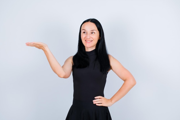 Une jeune fille souriante lève les yeux et pointe vers la gauche avec la main sur fond blanc