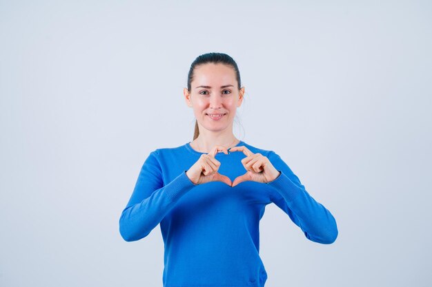 Une jeune fille souriante montre un geste cardiaque sur fond blanc