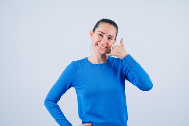 Jeune fille souriante montre un geste mobile avec la main sur fond blanc