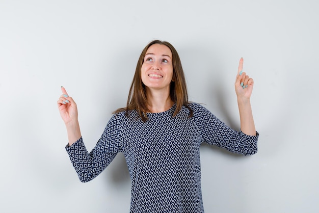 Une jeune fille souriante pointe ses doigts vers le haut sur un fond blanc