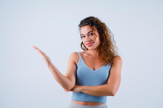 Jeune fille souriante pointe vers la gauche avec la main sur fond blanc