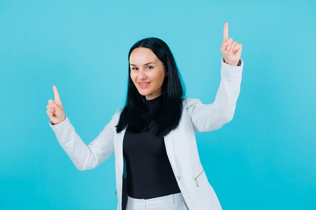 Jeune fille souriante pointe vers le haut avec les index sur fond bleu