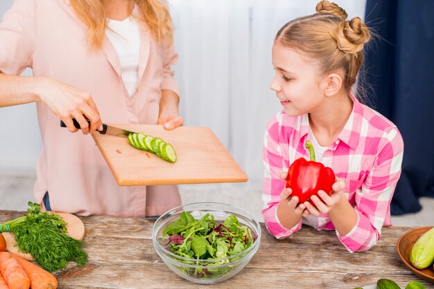 Jeune fille souriante regardant sa mère préparant la salade sur table