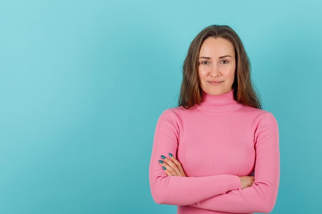 Une jeune fille souriante regarde la caméra en croisant les bras sur fond bleu