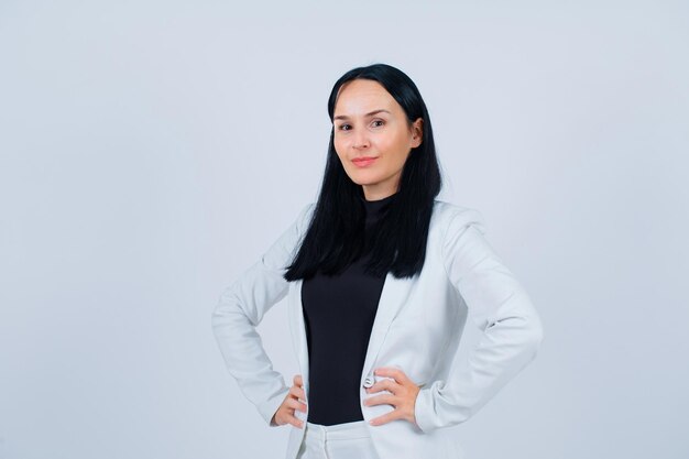 Jeune fille souriante regarde la caméra en mettant les mains sur la taille sur fond blanc