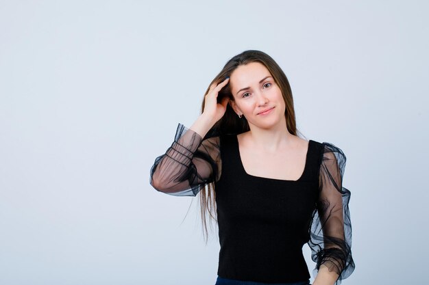 Jeune fille souriante regarde la caméra en tenant la main sur la tête sur fond blanc