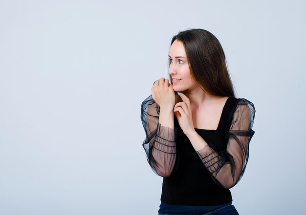 Jeune fille souriante regarde à gauche en se tenant la main sous le menton sur fond blanc