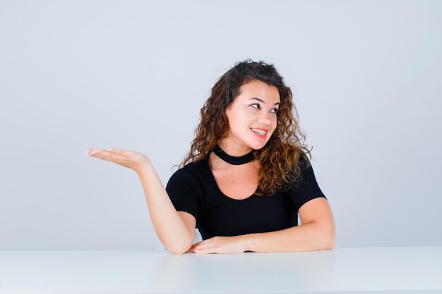 Jeune fille souriante regarde vers le haut et pointe vers la gauche avec la main sur fond blanc