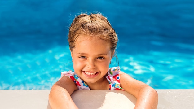 Jeune fille souriante se tenant au bord de la piscine et regardant la caméra