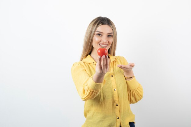 Jeune fille souriante tenant une tomate rouge sur blanc.