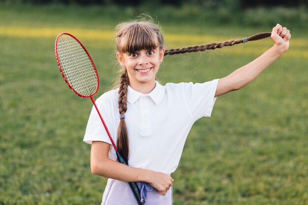 Jeune fille souriante tirant ses longs cheveux tressés tenant du badminton