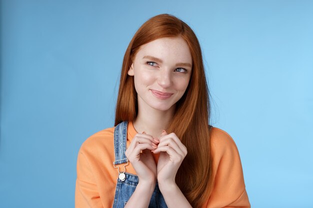 Une jeune fille sournoise et délicate a un excellent plan, un sourire narquois ravi, un regard mystérieux dans le coin supérieur gauche, souriant, a une idée qui tourne pensivement les doigts debout, se réjouissant d'un fond bleu