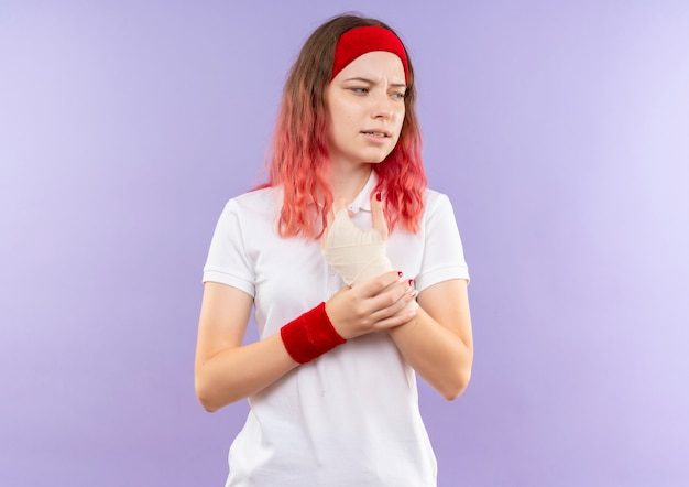 Jeune fille sportive touchant son poignet bandé sensation de douleur debout sur un mur violet