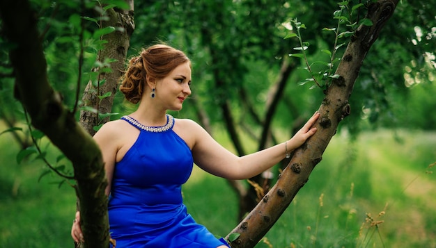 Jeune fille en surpoids à la robe bleue posée fond jardin de printemps assis sur l'arbre