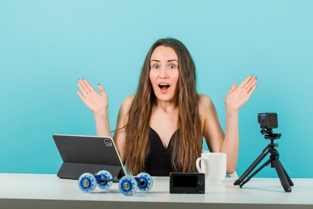 Une jeune fille surprise ouvre grand ses mains devant la caméra sur fond bleu