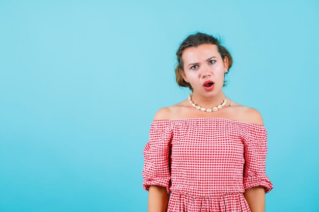 Une jeune fille surprise regarde la caméra en ouvrant la bouche sur fond bleu