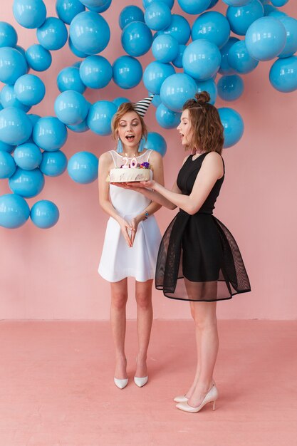Jeune fille surprise tenant un gâteau d&#39;anniversaire et son amie debout à proximité.