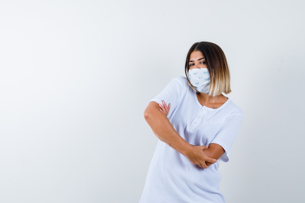 Jeune fille en t-shirt blanc et masque debout les bras croisés et regardant confiant, vue de face.