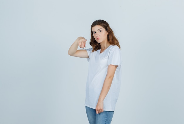 Jeune fille en t-shirt blanc pointant vers la caméra et regardant sensible, vue de face.