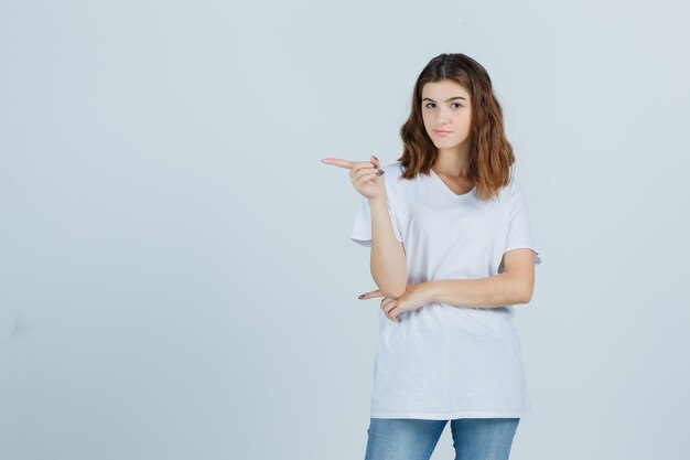 Jeune fille en t-shirt blanc pointant vers le côté gauche et regardant pensif, vue de face.