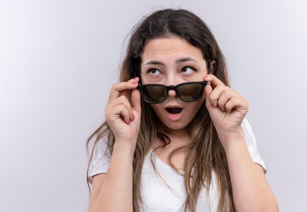 Jeune fille en t-shirt blanc remettant des lunettes à choqué avec la bouche grande ouverte