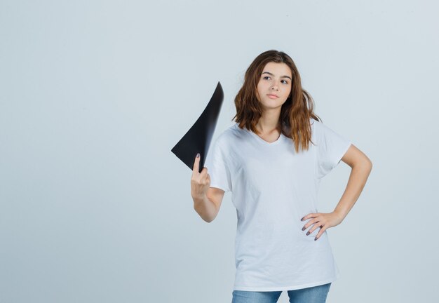 Jeune fille en t-shirt blanc tenant le dossier et regardant pensif, vue de face.