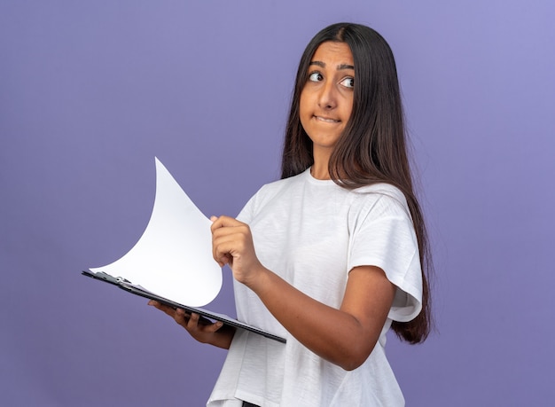 Jeune fille en t-shirt blanc tenant le presse-papiers avec des pages blanches jusqu'à perplexe