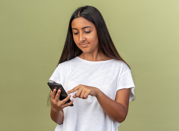 Jeune fille en t-shirt blanc tenant un smartphone écrivant un message à la confiance debout sur fond vert