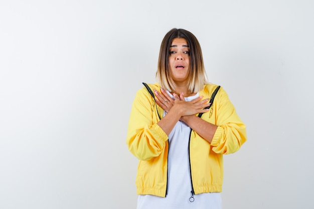 Jeune fille en t-shirt blanc, veste jaune croisant deux bras sur la poitrine et regardant excité, vue de face.