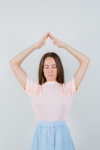 Jeune fille en t-shirt faisant un geste de toit de maison au-dessus de la tête et à la vue de face, heureux.