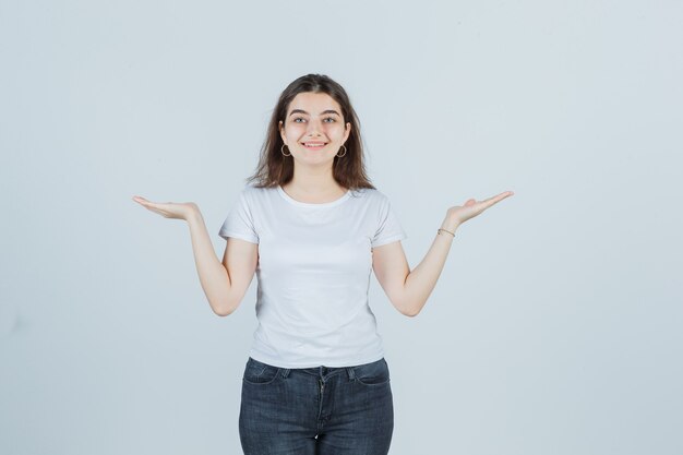 Jeune fille en t-shirt, jeans étalant les paumes et à la vue de face, heureux.