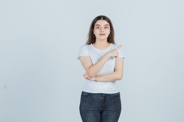 Jeune fille en t-shirt, jeans pointant de côté et à la vue réfléchie, de face.