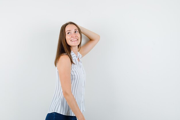 Jeune fille en t-shirt, jeans posant avec la main sur la tête et l'air heureux.